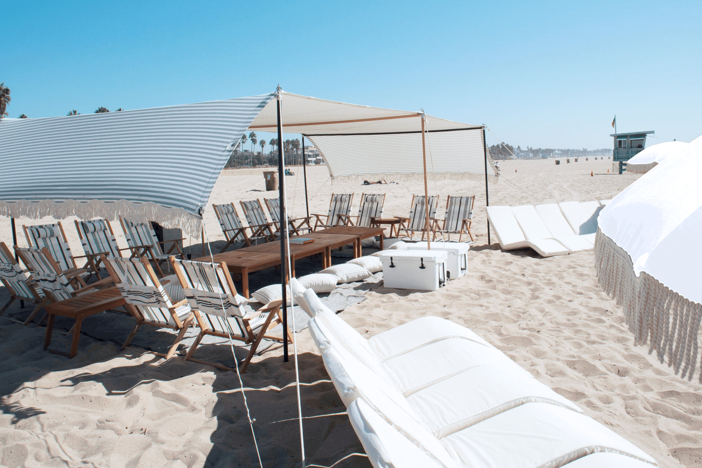 Large beach cabana rental with white beach lounges, beach umbrellas in Santa Monica, Los Angeles