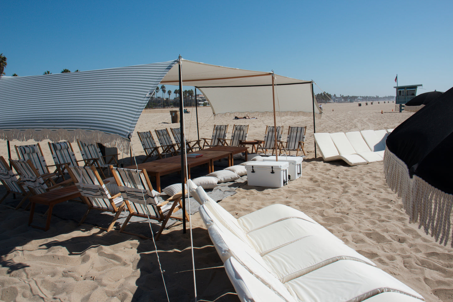 Large beach cabana rental with white beach lounges, beach umbrellas in Santa Monica, Los Angeles